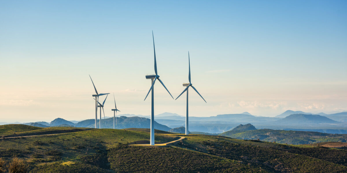 Aerogeneradores en un paisaje montañoso, con un cielo azul despejado y cordilleras distantes al fondo. La escena transmite tranquilidad y generación de energía sostenible.