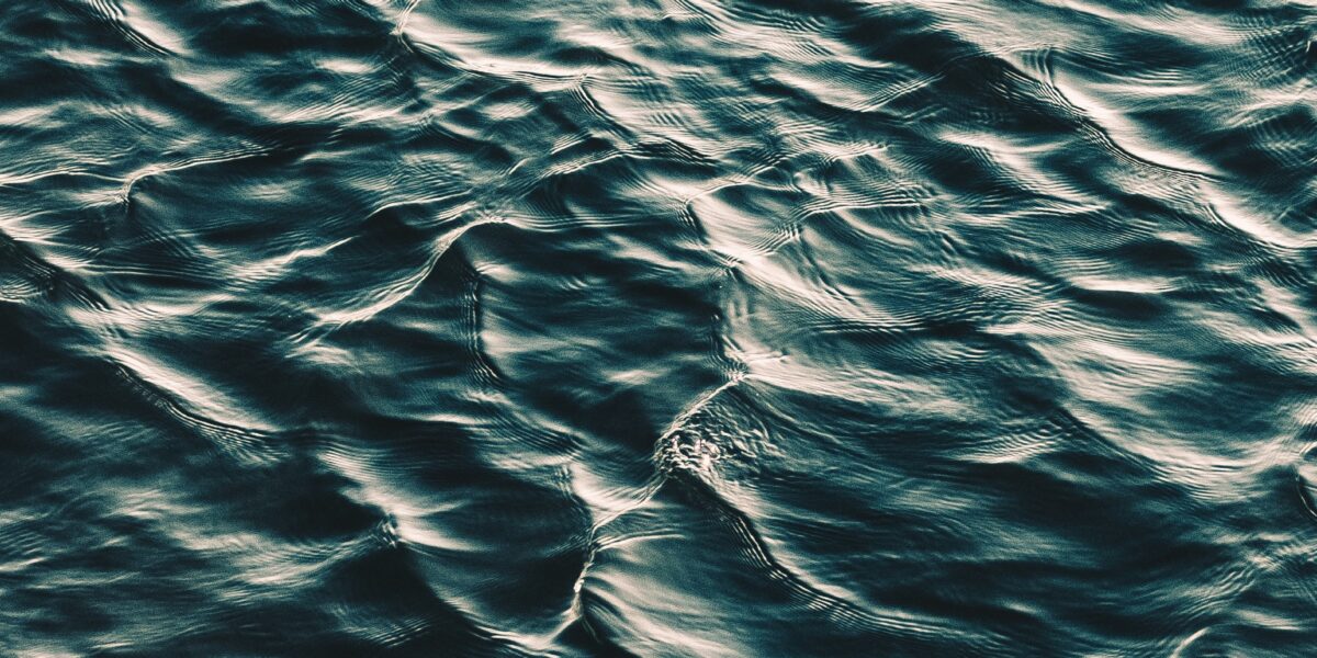 Un primer plano de las oscuras olas del océano, que captura la textura y el movimiento del agua. La superficie refleja la luz, creando un patrón de luces y sombras sobre las ondulantes olas.