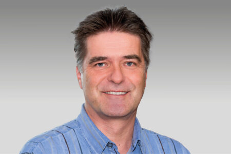 Hombre sonriente con una camisa de cuello azul claro sobre un fondo degradado gris.