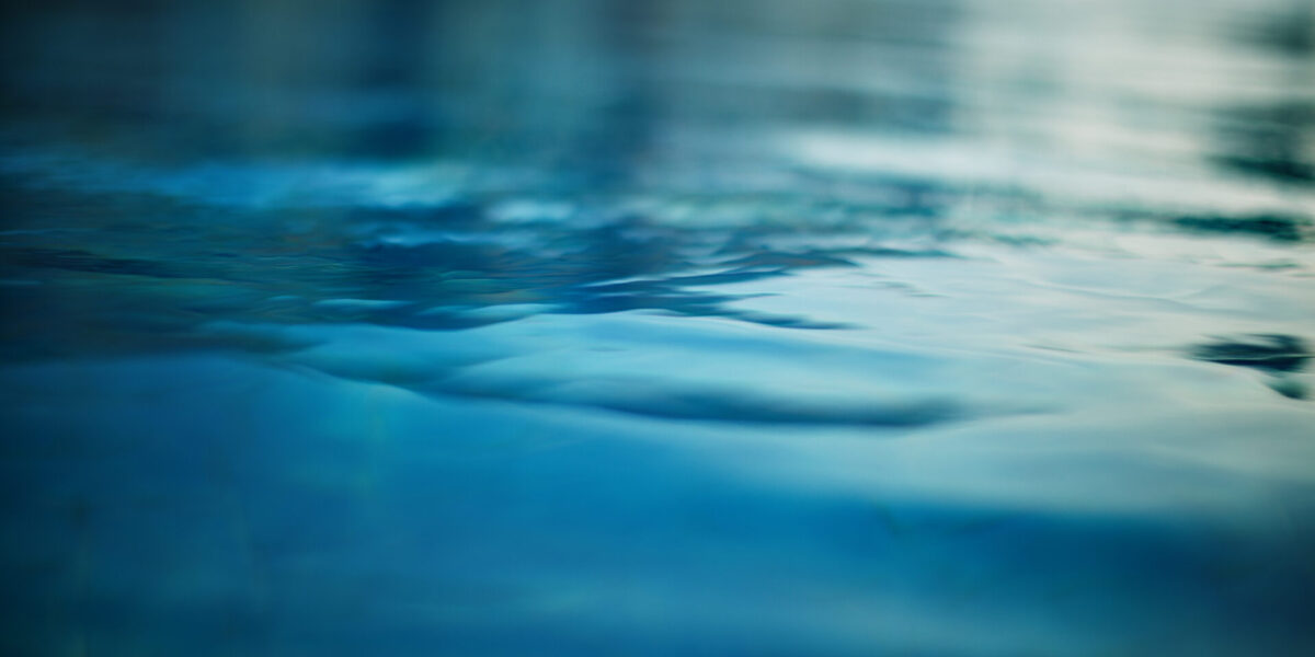 Primer plano de aguas tranquilas y ondulantes con diferentes tonos de azul y verde, que reflejan una luz tenue. La superficie luce lisa y serena, evocando una sensación de tranquilidad.