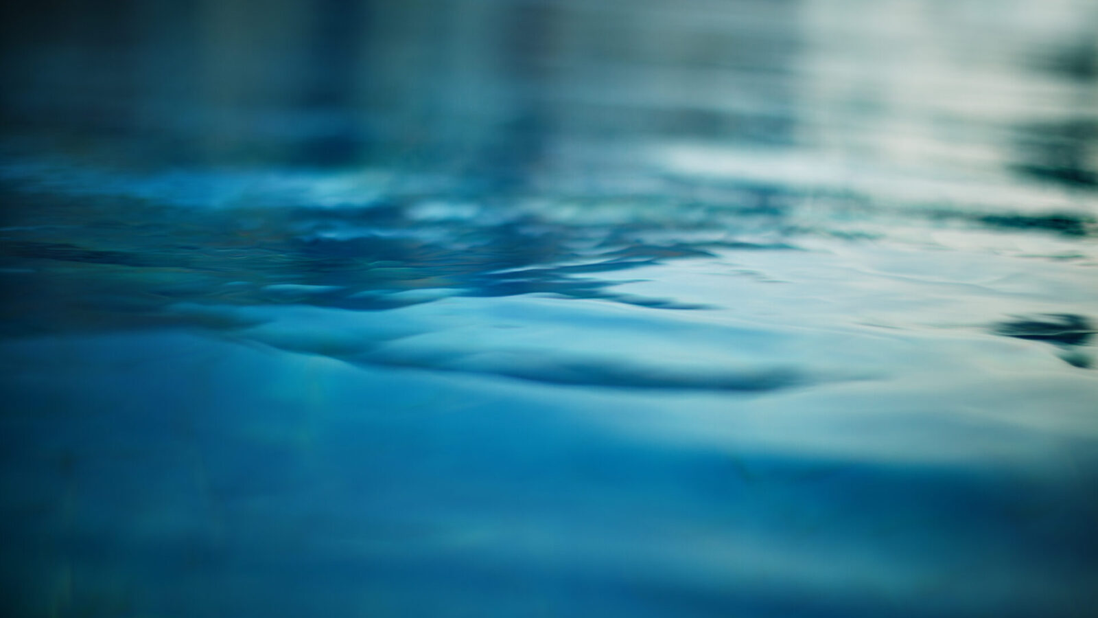 Primer plano de aguas tranquilas y ondulantes con diferentes tonos de azul y verde, que reflejan una luz tenue. La superficie luce lisa y serena, evocando una sensación de tranquilidad.