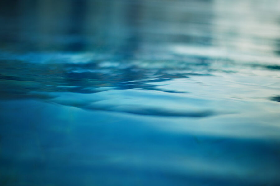 Primer plano de aguas tranquilas y ondulantes con diferentes tonos de azul y verde, que reflejan una luz tenue. La superficie luce lisa y serena, evocando una sensación de tranquilidad.