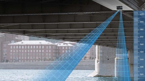 Vista de un puente sobre el agua con un sensor de altura que proyecta rayos azules, midiendo la distancia hasta la superficie del agua. A la derecha se muestra una escala de medición, con un edificio visible al fondo.