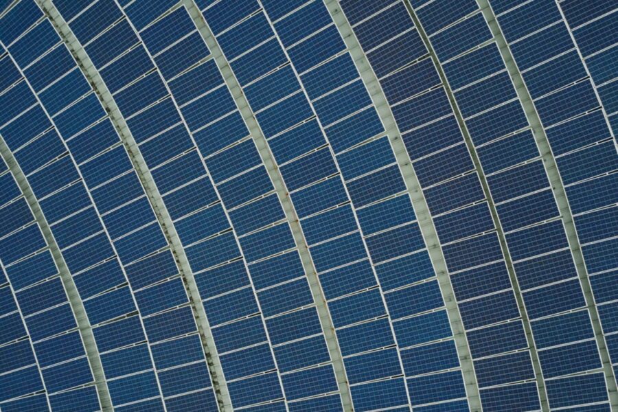 Vista aérea de filas de paneles solares azules dispuestos en un patrón arqueado. Los paneles forman parte de un parque solar más grande, diseñado para captar la luz solar y generar energía renovable. La estructura repetitiva crea un atractivo patrón geométrico.