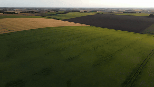 Aerial view of wide, open farmland with green and yellow fields under a hazy sky, as the camera smoothly pans over the rural landscape.
